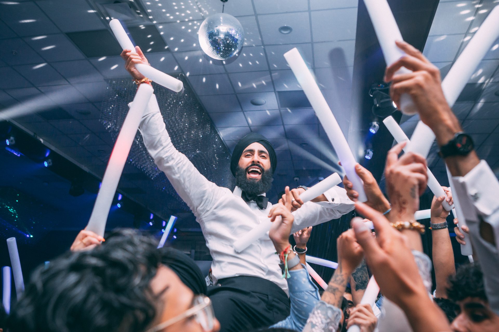 Packed dance floor for wedding reception with special effects like glow sticks, sparklers and low laying fog.
